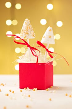 Cake pops made of fondant sticking in red gift box. Very shallow depth of field and Christmas lights in the background