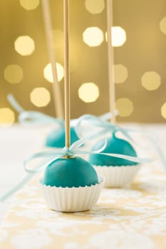 Turquoise Christmas cake pops sticking upside down in miniature cupcake liners. Very shallow depth of field with Christmas lights in the background