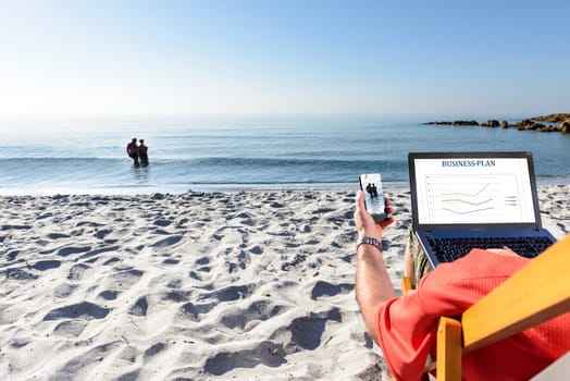 Businessman on the beach working with notebook and smartphone