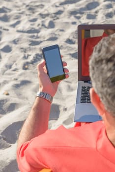 Businessman on the beach working with notebook and smartphone