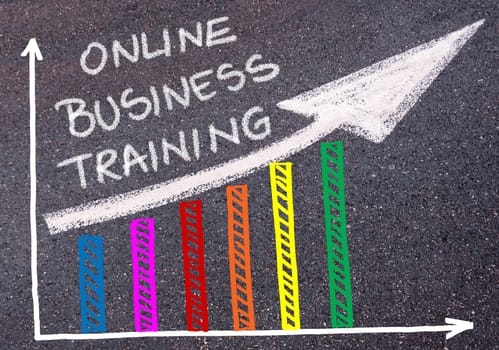 ONLINE BUSINESS TRAINING written with chalk on tarmac over colorful graph and rising arrow, business marketing and creativity concept
