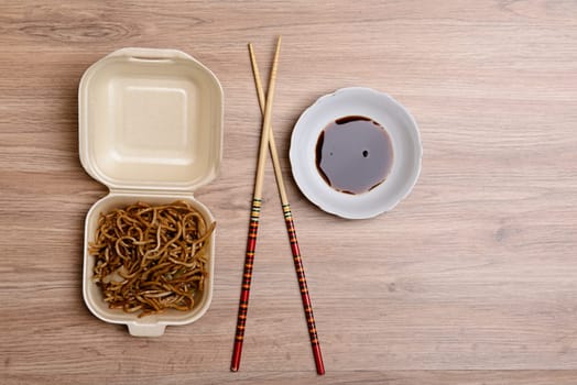 chinese nooles in box with chopsticks and soy sauce on wooden ground from above
