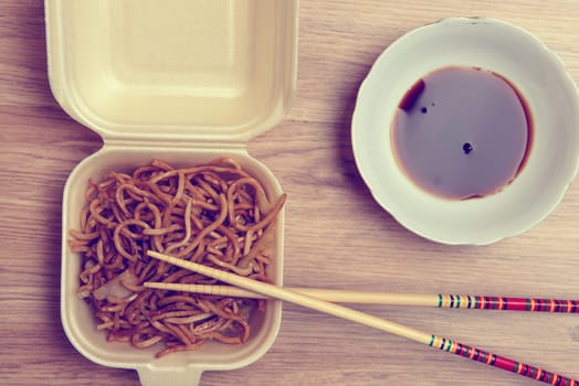 chinese nooles in box with chopsticks and soy sauce on wooden ground from above