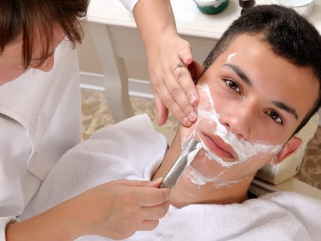 Shaving at the barber of a young boy in retro style with razor and shaving soap