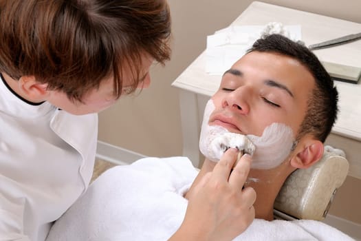 Shaving at the barber of a young boy in retro style with razor and shaving soap