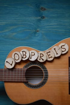 Guitar on blue-green wood with individual wooden discs on it,which form the word: PRAISE
