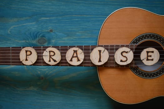 Guitar on blue-green wood with individual wooden discs on it,which form the word: PRAISE
