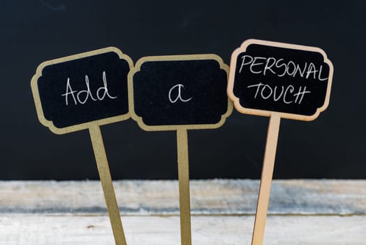 Business message ADD A PERSONAL TOUCH written with chalk on wooden mini blackboard labels, defocused chalkboard and wood table in background