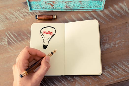Retro effect and toned image of a woman drawing a lighting bulb with fountain pen on a notebook. STRATEGY symbol and concept, copy space available for text