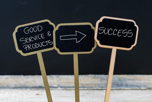 Business message GOOD SERVICE AND PRODUCTS LEAD TO SUCCESS written with chalk on wooden mini blackboard labels, defocused chalkboard and wood table in background