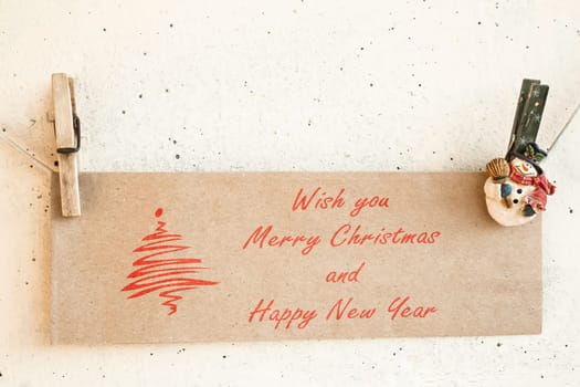 Christmas snowman clothespins hanging on clothesline or rope and holding greeting card card on plaster background
