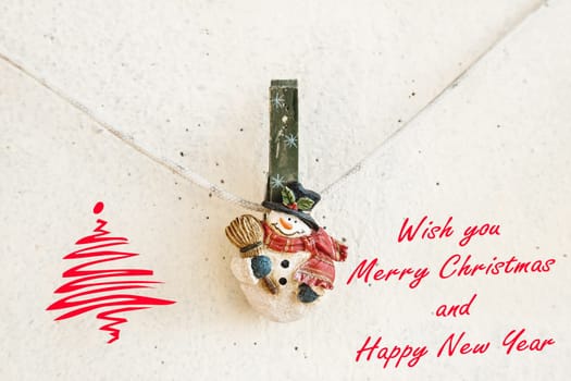 Christmas greeting card with snowman clothespin hanging on clothesline or rope on plaster background