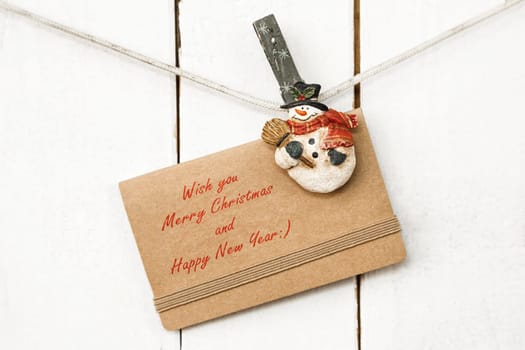 Christmas snowman clothespins hanging on clothesline or rope and holding greeting card on wooden background