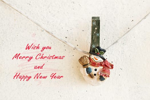 Christmas greeting card with snowman clothespin hanging on clothesline or rope on plaster background