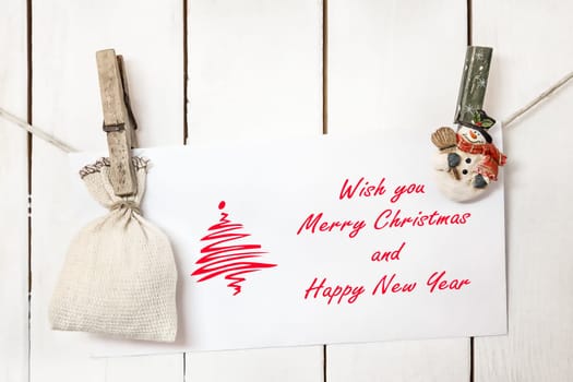 Christmas snowman clothespins hanging on clothesline or rope and holding Christmas greeting card and sack on wood background