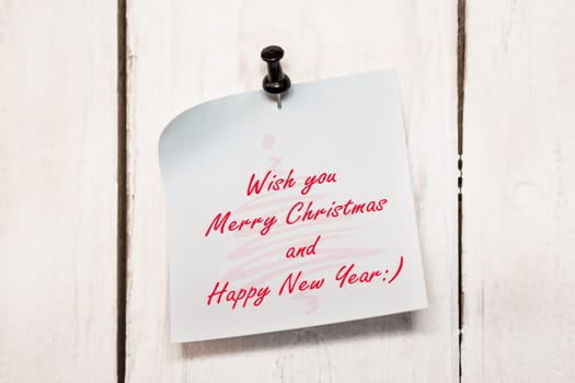Light blue Christmas greeting note paper with push black pin on wood background