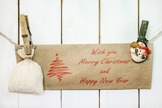Christmas snowman clothespins hanging on clothesline or rope and holding brown Christmas greeting card and sack on wood background