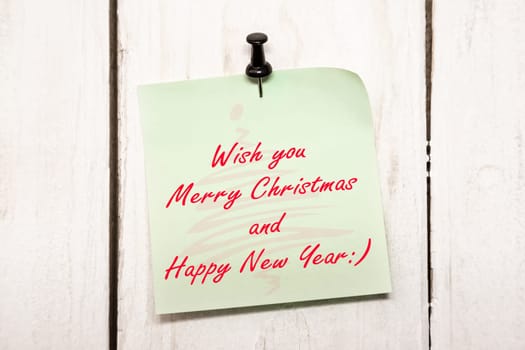 Light green Christmas greeting note paper with push black pin on wood background