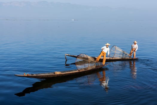 Myanmar travel attraction landmark - Traditional Burmese fishermen with fishing net at Inle lake in Myanmar famous for their distinctive one legged rowing style
