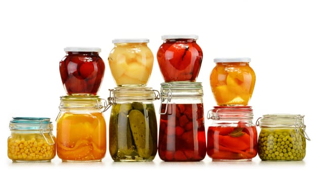 Jars with pickled vegetables and fruity compotes isolated on white background. Preserved food