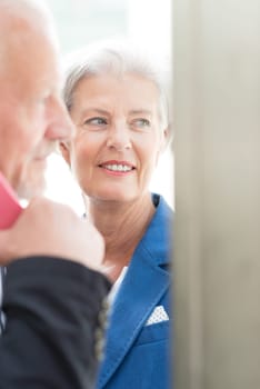 Two seniors stand at a public telephone booth and make phone calls