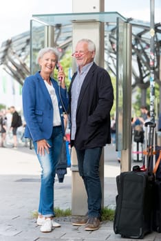 Two seniors stand at a public telephone booth and make phone calls