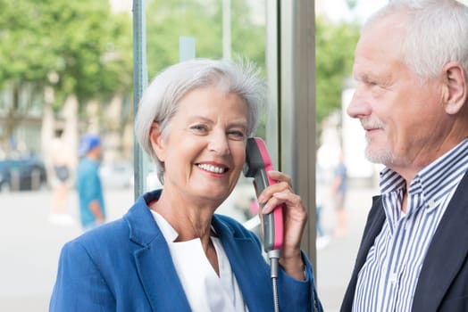 Two seniors stand at a public telephone booth and make phone calls