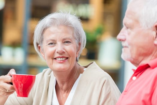 Two smiled seniors sit in a café and drink from a red cup