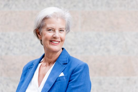 Smiling senior citizen with gray hair in front of a wall