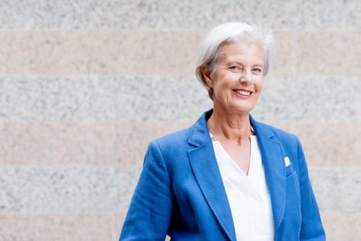 Smiling senior citizen with gray hair in front of a wall