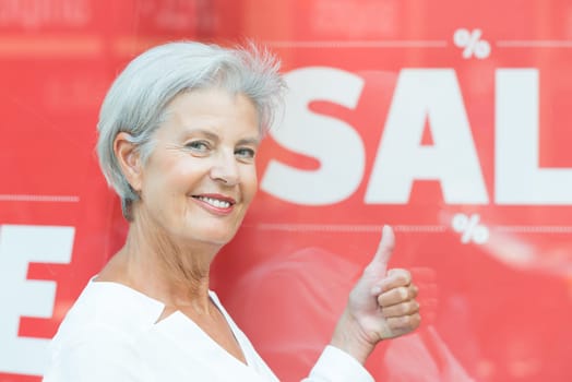 Smiling senior citizen in front of a shop window with a sale sign