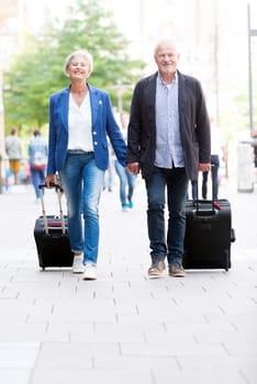 Two seniors with suitcases on a sidewalk
