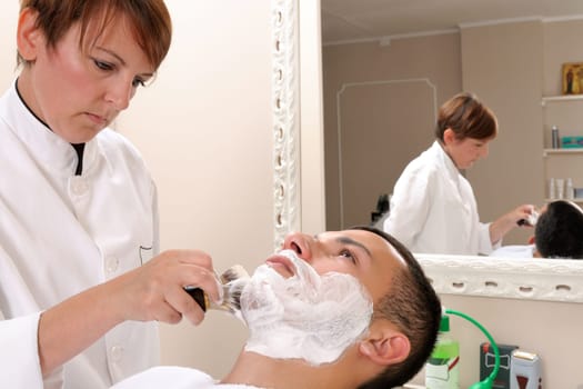 Shaving at the barber of a young boy in retro style with razor and shaving soap
