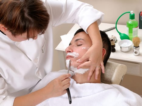 Shaving at the barber of a young boy in retro style with razor and shaving soap