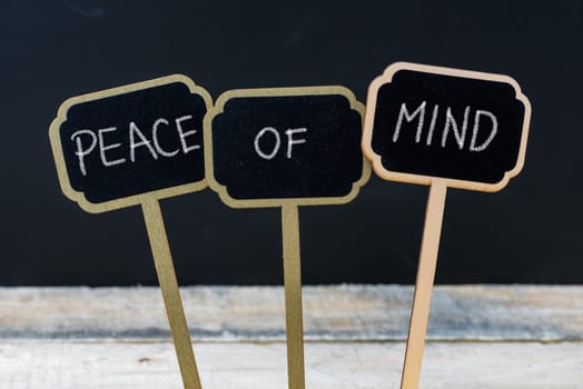 Business message PEACE OF MIND written with chalk on wooden mini blackboard labels, defocused chalkboard and wood table in background