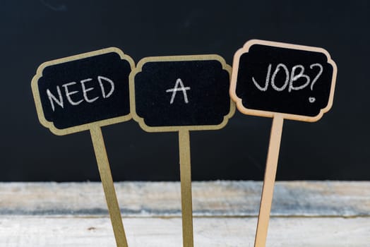 Business message NEED A JOB ? written with chalk on wooden mini blackboard labels, defocused chalkboard and wood table in background