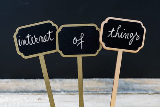 Business message INTERNET OF THINGS written with chalk on wooden mini blackboard labels, defocused chalkboard and wood table in background