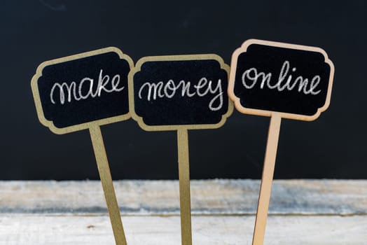 Business message MAKE MONEY ONLINE written with chalk on wooden mini blackboard labels, defocused chalkboard and wood table in background