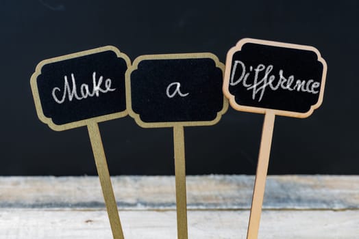 Business message MAKE A DIFFERENCE written with chalk on wooden mini blackboard labels, defocused chalkboard and wood table in background