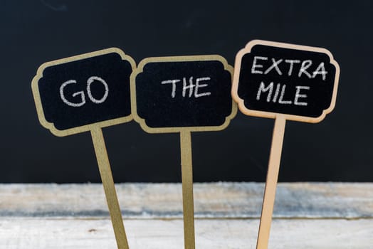 Business message GO THE EXTRA MILE written with chalk on wooden mini blackboard labels, defocused chalkboard and wood table in background