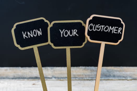 Business message KNOW YOUR CUSTOMER written with chalk on wooden mini blackboard labels, defocused chalkboard and wood table in background