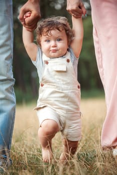 Young beautiful father, mother and little toddler son against green trees. Happy family with her baby boy on a summer sunny day. Family walking on the meadow.
