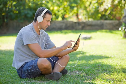 young man relaxing with a tablet pc listening music with headphones on a the park, outdoor