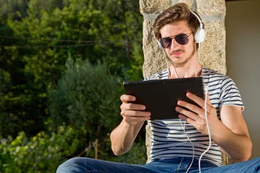 young man relaxing with a tablet pc listening music with headphones, outdoor