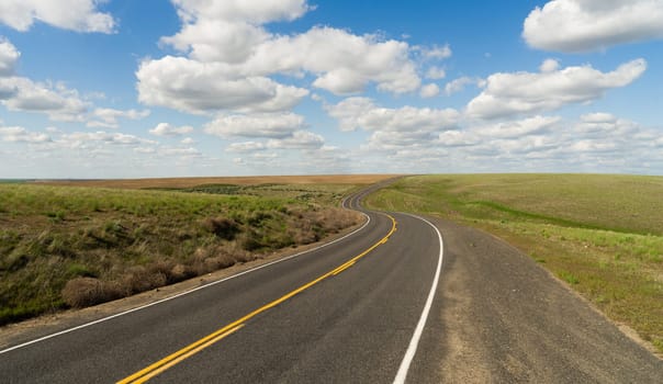 A central Washington State road winds out into the distance below fluffy blue clouds