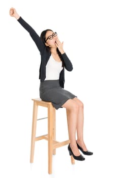 Full body portrait of young Asian woman yawning, sitting on high chair, isolated on white background.