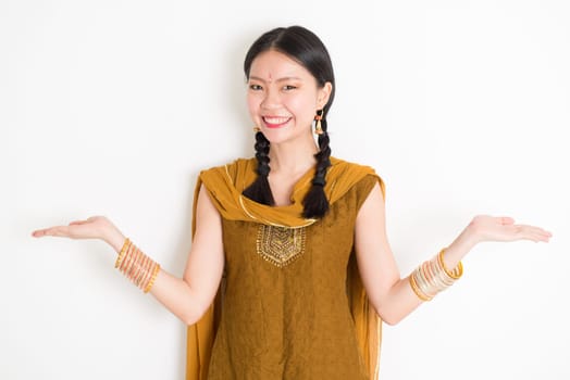 Portrait of young mixed race Indian Chinese woman in traditional punjabi dress hands showing somethings, standing on plain white background.