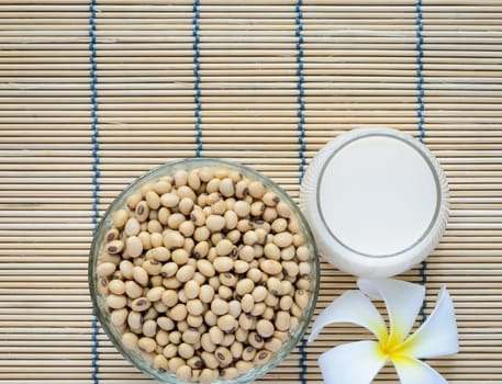 Fresh Soy milk (Soya milk) and dried soybean seeds on bamboo place mat with white plumeria flower. Traditional staple of East Asian cuisine