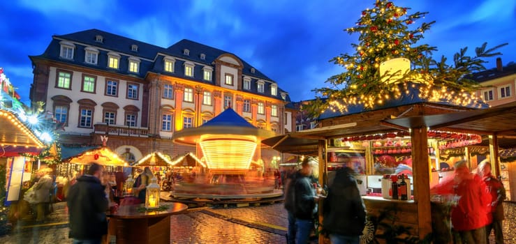 Christmas market in Heidelberg,Germany,a panorama shot at dusk showing illuminated kiosks,architecture and blurred people