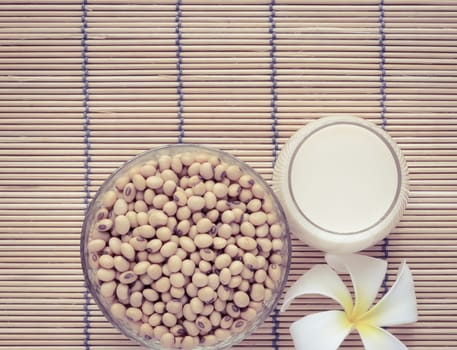 Fresh Soy milk (Soya milk) and dried soybean seeds on bamboo place mat with white plumeria flower. Retro-Vintage filter effect